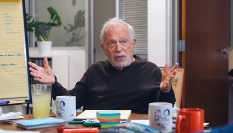 In an image from the new documentary "The Work in Progress," executive producer Robert Reich sits at a work table gesturing earnestly as he talks.
