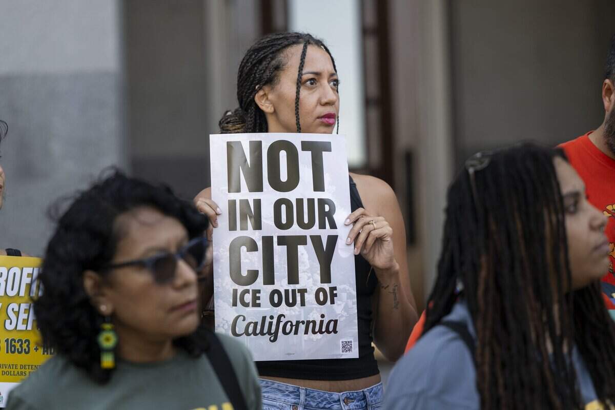 Christina Livingston of Sacramento holds a sign while joining supporters and political leaders during a rally on the west steps of the state Capitol on Tuesday urging the governor to sign two Assembly bills targeting the profitability of corporations involved in immigration detention and deportation.