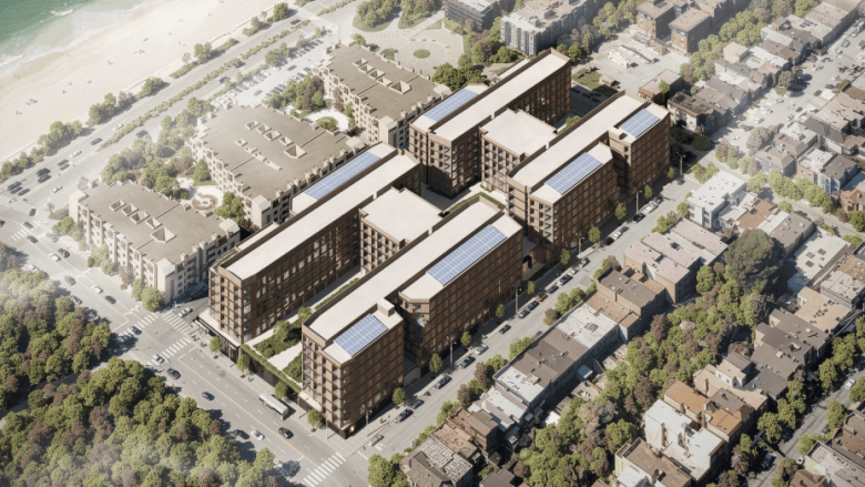 Aerial view of a large apartment complex with solar panels on the roofs, surrounded by residential buildings, roads, trees, and a beach nearby.