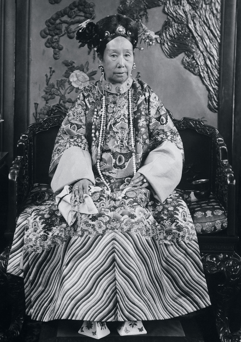 Black-and-white portrait of Empress Dowager Cixi in ornate Qing dynasty robes and headdress, seated formally in a carved chair, dignified.