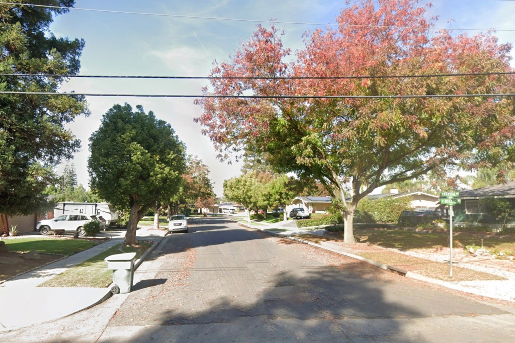 Residential street with cars parked on the side, surrounded by houses and trees with changing fall foliage.
