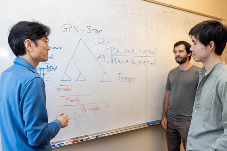 Three people discuss a problem that is written on a white board.