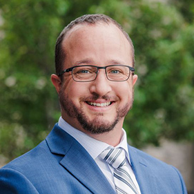 A man in a blue suit with tie, smiles