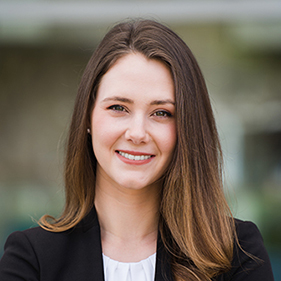 A woman with medium-length dark hair and a dark suit smiles. 