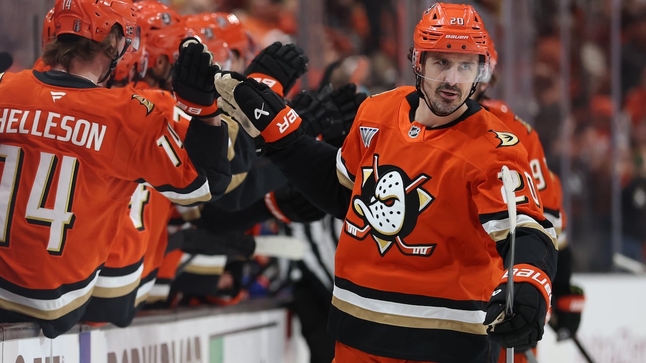 A male ice hockey player touches gloves with teammates in celebration as he skates past the bench during a game.
