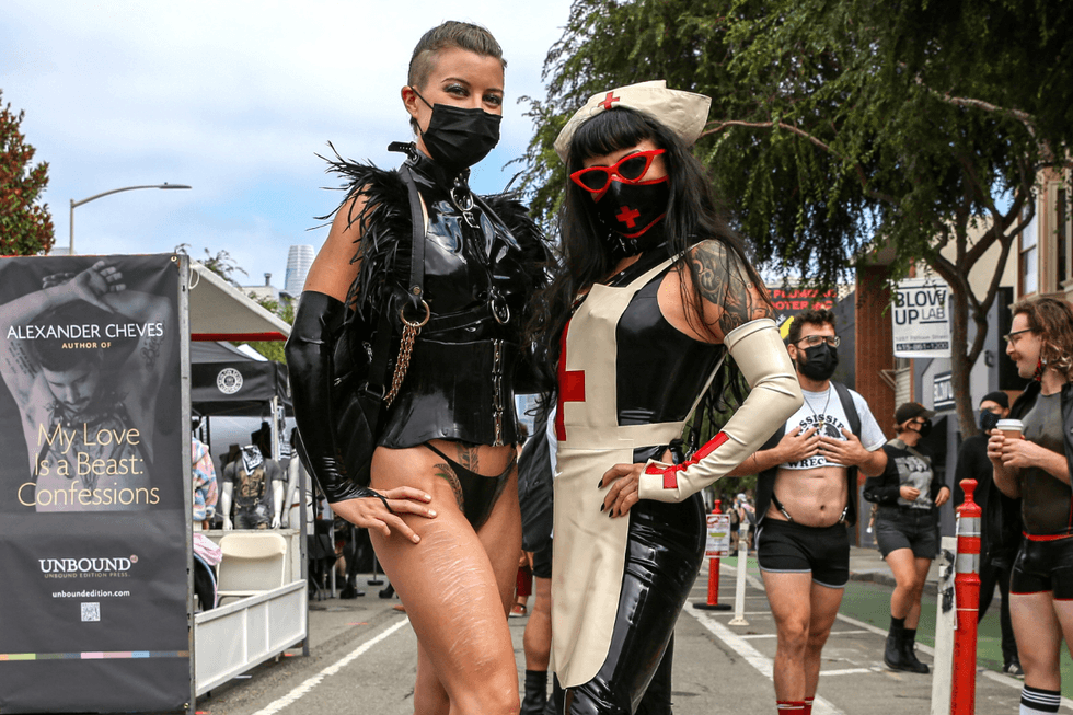 Folsom Street Fair attendees pose in fetishwear in San Francisco. A banner for Alexander Cheves\u2019s My Love Is a Beast: Confessions appears in the background.