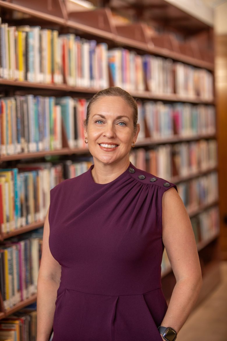 A portrait photo of a woman standing in front of a shelf lined with books
