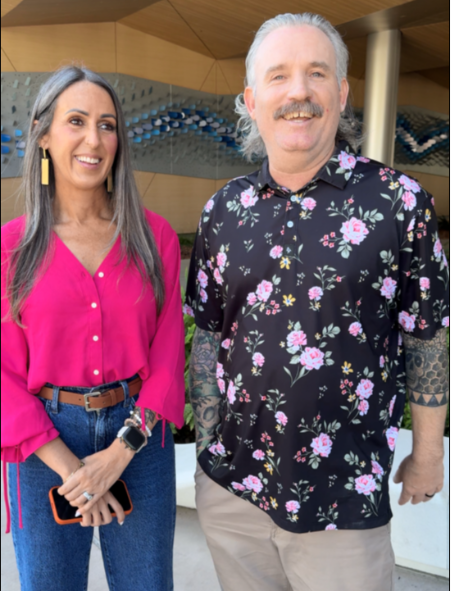 Two people stand outside a building, posing for a photo together.
