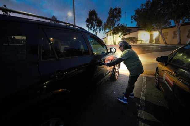 Parked at a park in Linda Vista, Adriana Jasso places the magnetic door signage identifying their group. The small group of volunteers with the Unión del Barrio community patrol will drive through alleyways and large parking lots, as well as past nearby schools, searching for signs indicating that federal immigration agents are actively operating in the area. (Nelvin C. Cepeda / The San Diego Union-Tribune)