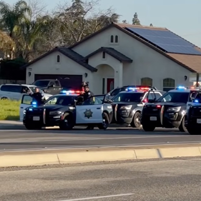 Row of Fresno Police Department cars with flashing lights outside a house.