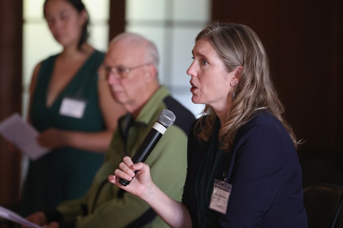 An attendee speaks into a microphone from her seat as others nearby listen.