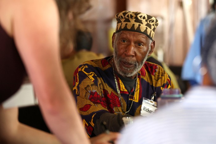 A participant in a patterned cap and printed shirt listens to someone across the table.