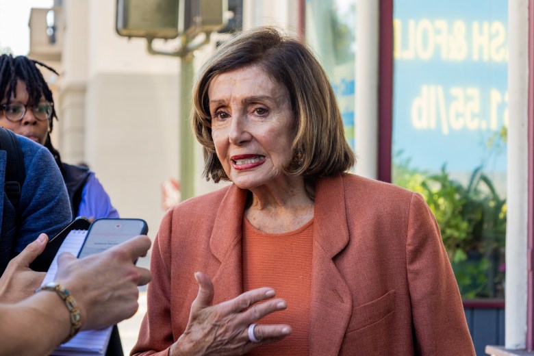 Nancy Pelosi speaking to reporters while holding a hand gesture.