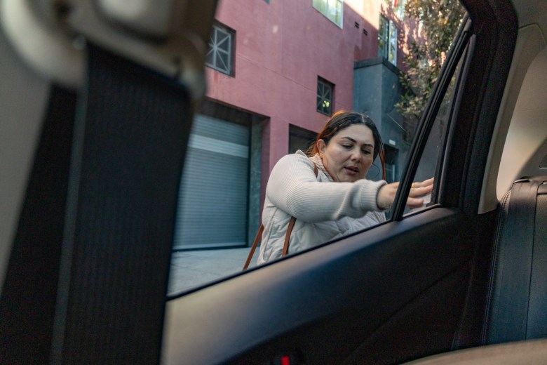 A San Francisco educator standing outside a car reaches through the open window to touch the interior.