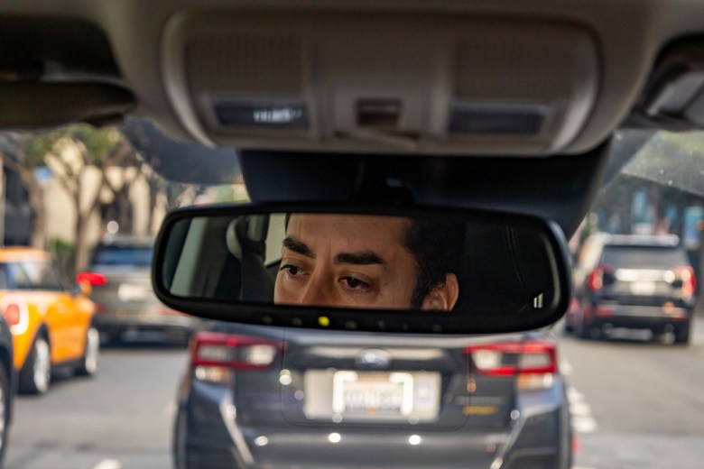 A San Francisco educator’s eyes and forehead reflected in a car rearview mirror, with traffic visible through the windshield.