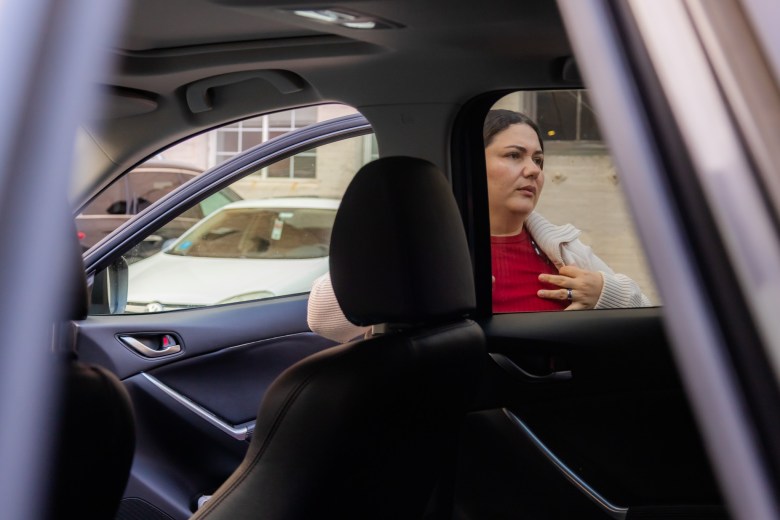 A San Francisco educator in a red shirt and white cardigan stands outside a car, looking through the open window.