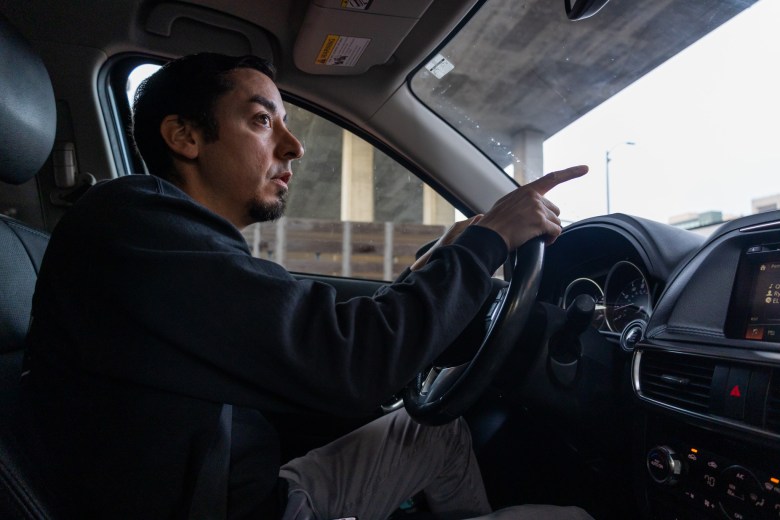 A San Francisco educator driving a car and pointing toward the view outside the windshield.