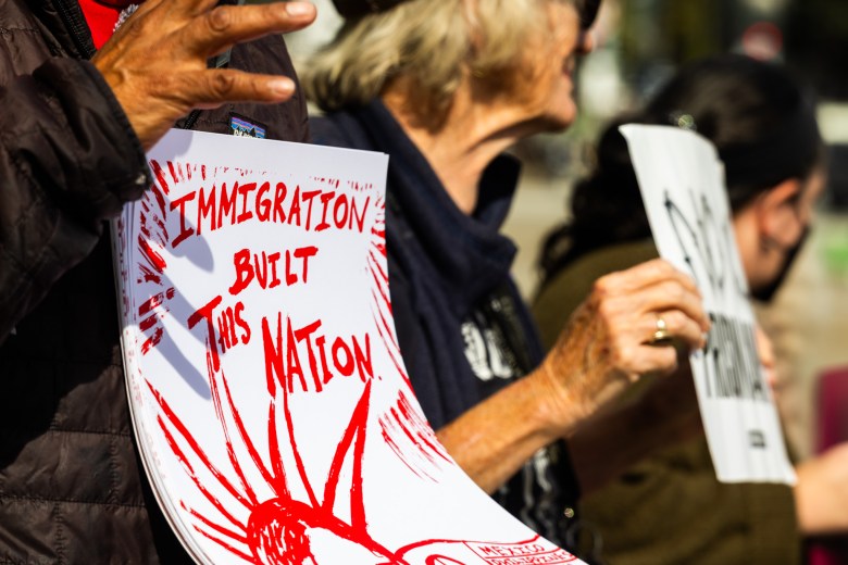 A person holds a sign that reads “IMMIGRATION BUILT THIS NATION” in red lettering.