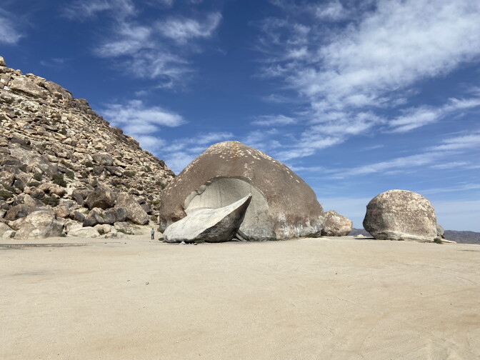 A giant boulder sits in the distance in the desert.