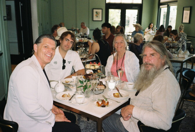 Three men and one woman dine at a restaurant with green walls.