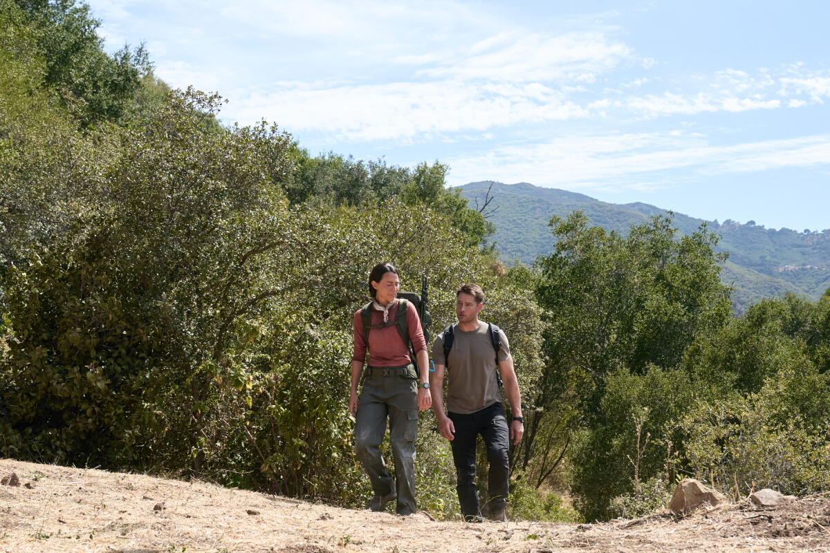 A woman and a man hike up a hill with trees behind them