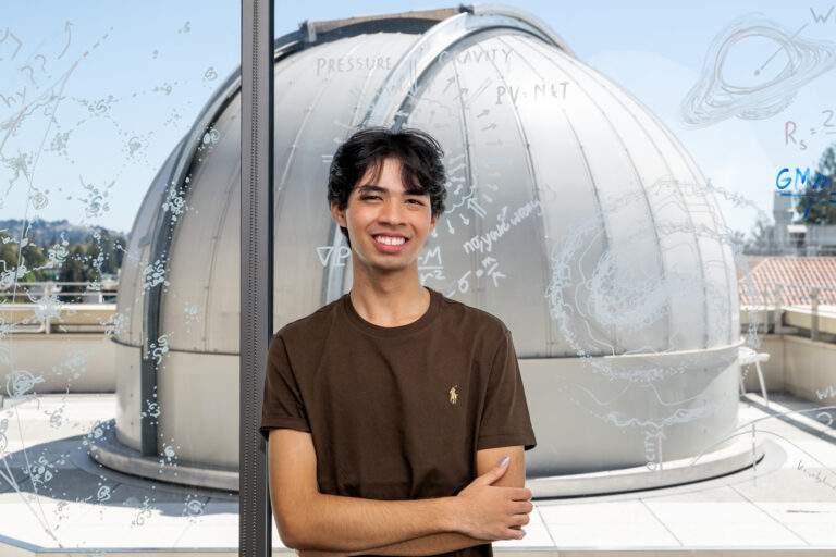 Julian Shapiro poses in front of a window overlooking an observatory