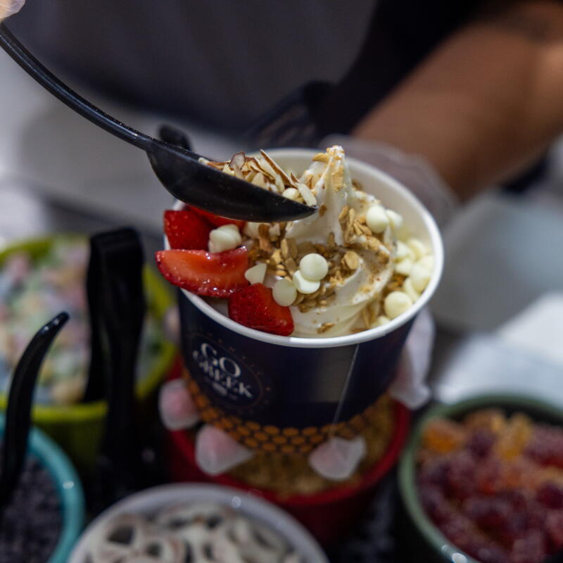 Fruit and nuts are added as toppings to a frozen Greek yogurt bowl.