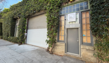 A gray door labeled "69" next to a large white roll-up garage door is framed by ivy-covered walls and frosted glass windows.