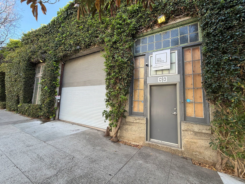 A gray door labeled "69" next to a large white roll-up garage door is framed by ivy-covered walls and frosted glass windows.