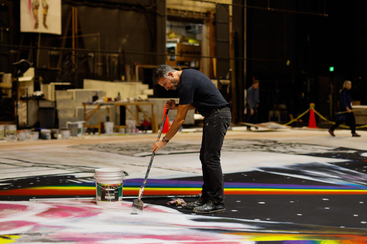 A man paints on a canvas on a stage.