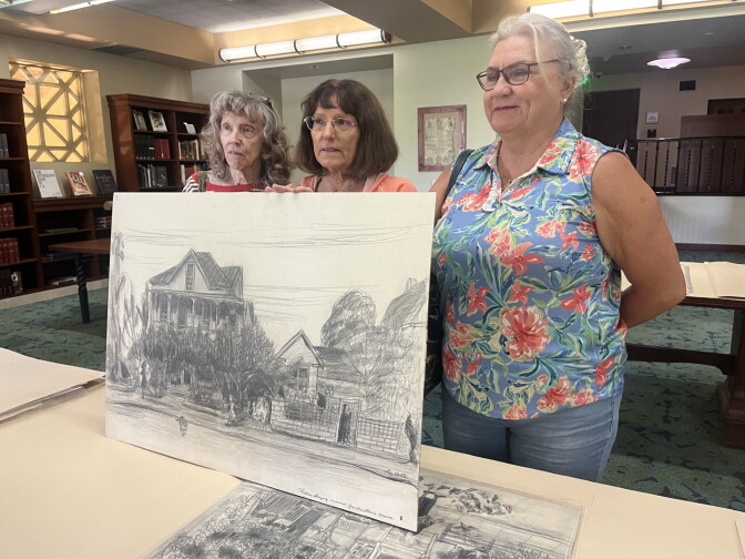 Three women standing in front of a drawing at a library.