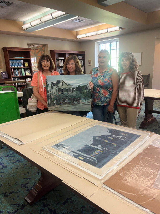 Four women in a library. One of them is holding a painting of the Bunker Hill home they lived in.