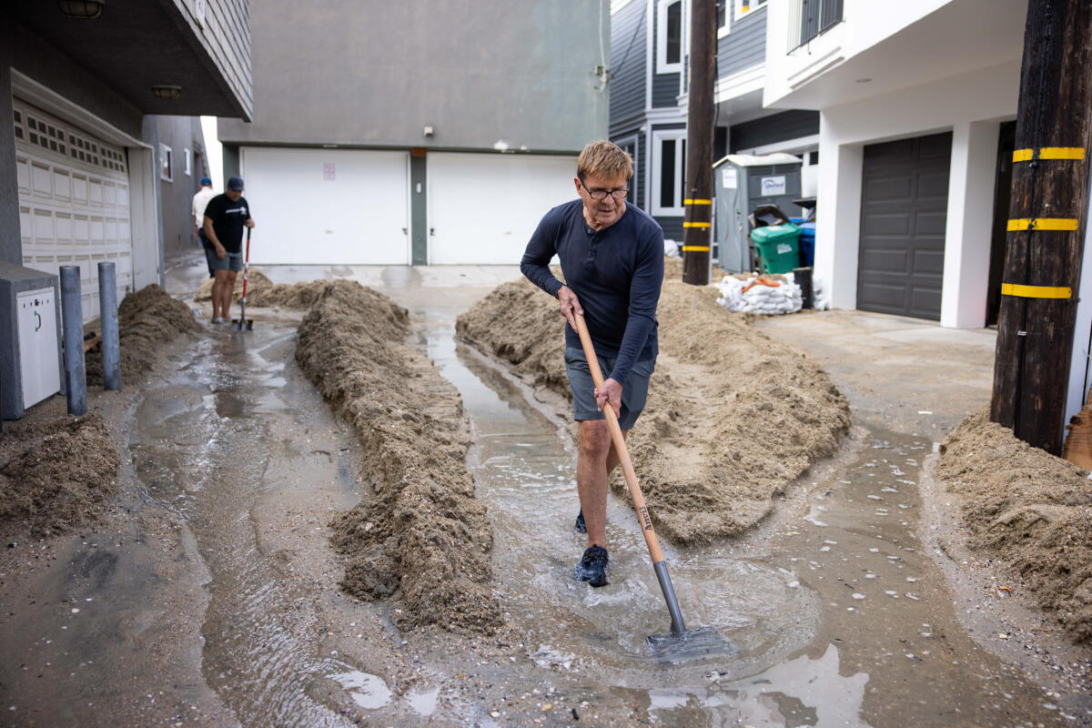 Robert Martin shovels a pathway out of sand for the water to flow at Peninsula in Long Beach on Sunday.