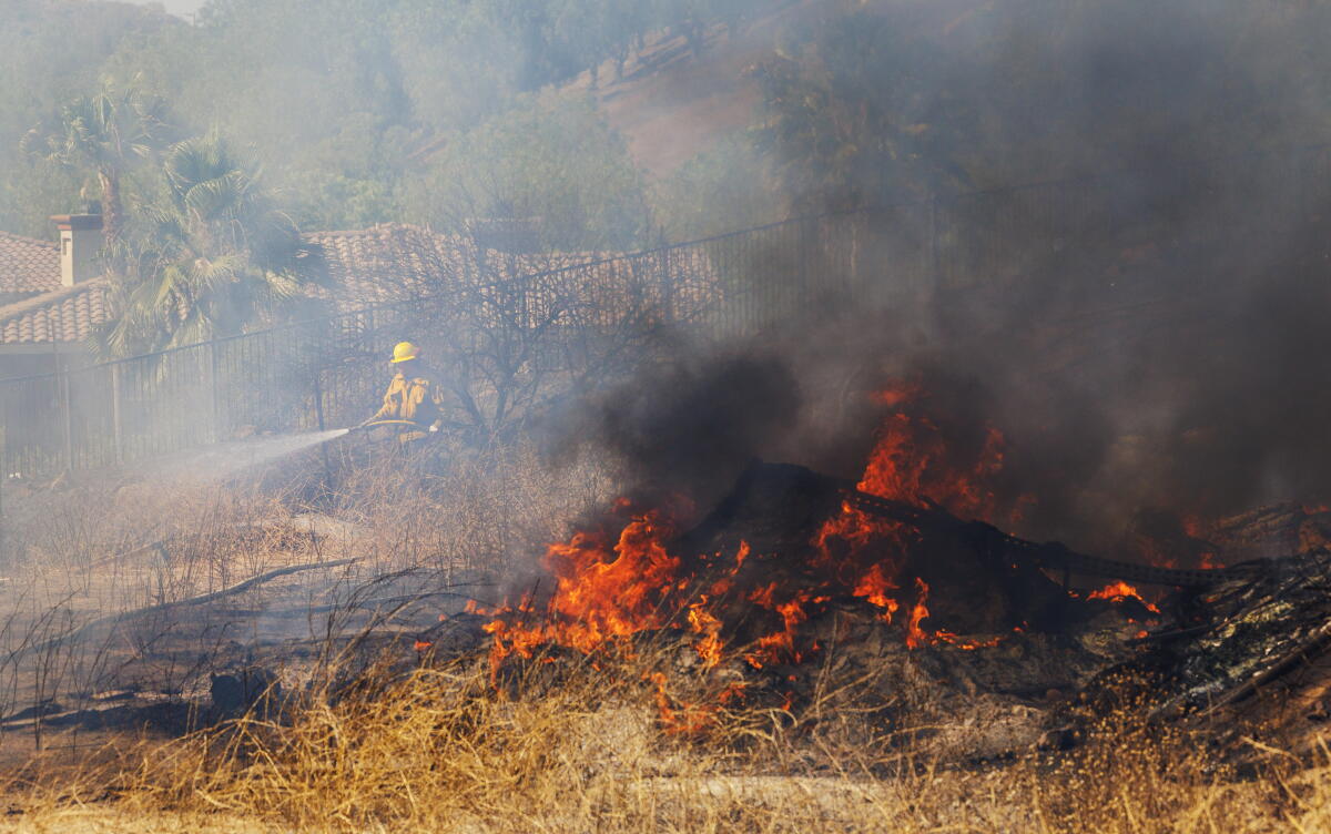 A firefighter keeps the ground wet behind homes in a field near Tampico Circle on June 24, 2024, in Corona