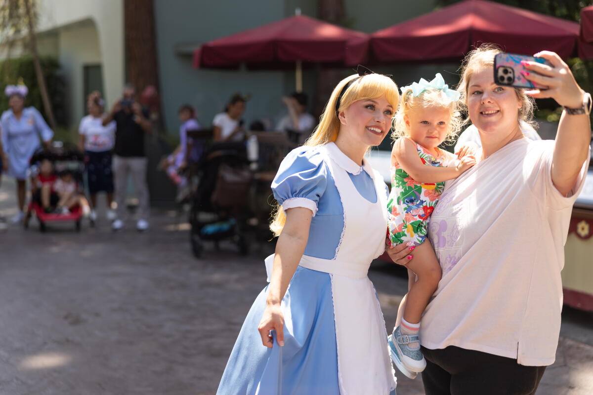 A Disneyland cast member playing the role of Alice in Wonderland interacts with guests.