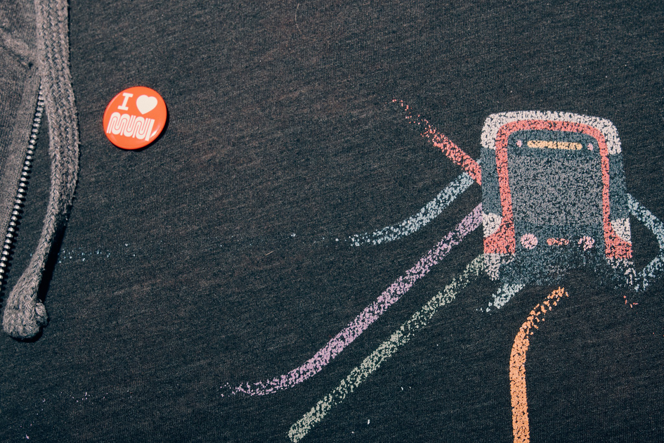 A dark hoodie features a red button reading "I ♥ MUJI" and a colorful stylized subway train graphic with lines representing tracks.