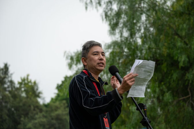 A man speaks into a microphone as he holds a piece of paper.