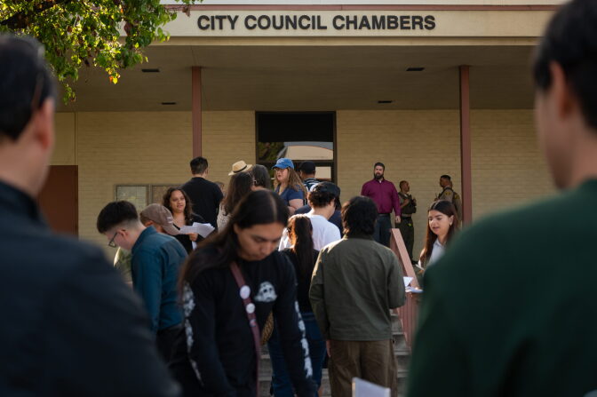 People stand in a line leading to a building up steps.