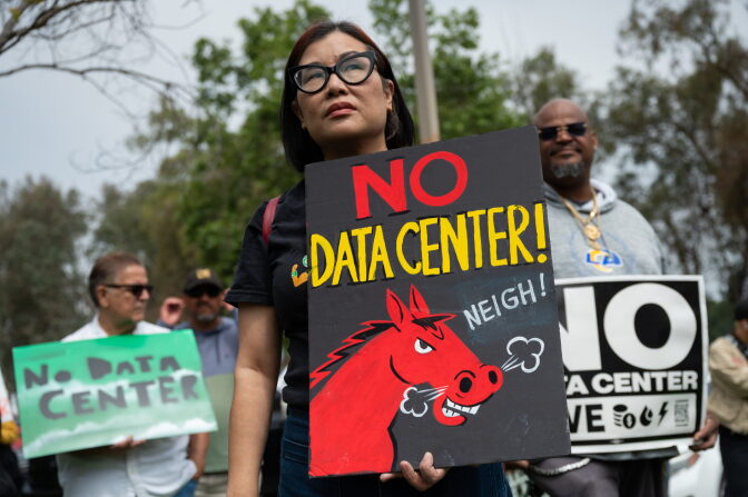 A woman holds a sign that reads "No data center!" with the illustration of a horse. Others behind her hold similar signage.