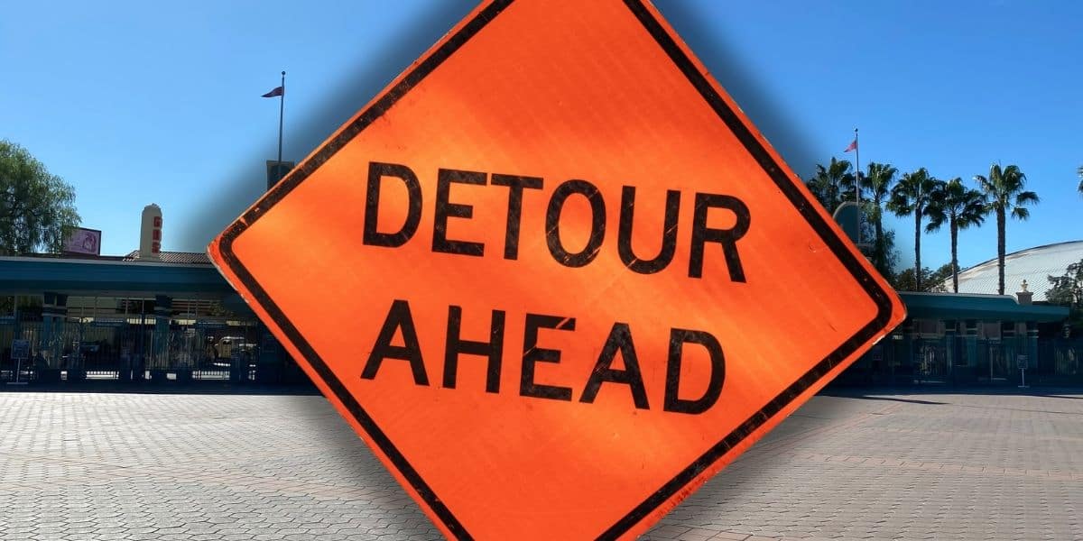 Orange "Detour Ahead" sign stands in front of an empty Disney California Adventure plaza lined with palm trees and attraction buildings inside of Disneyland Resort. Disney attraction closure.