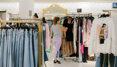 A woman in purple leggings and a gray tank top shops for dresses on racks in a well-lit clothing store with mirrors on the wall.