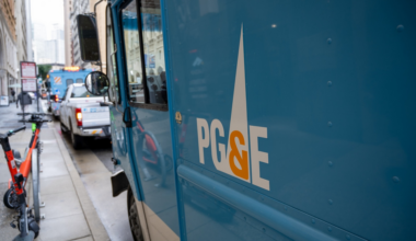 A blue PG&E utility truck is parked on a city street with electric scooters lined up on the sidewalk nearby.