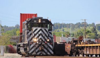 Black locomotive with white nose striping moves double-stack cars