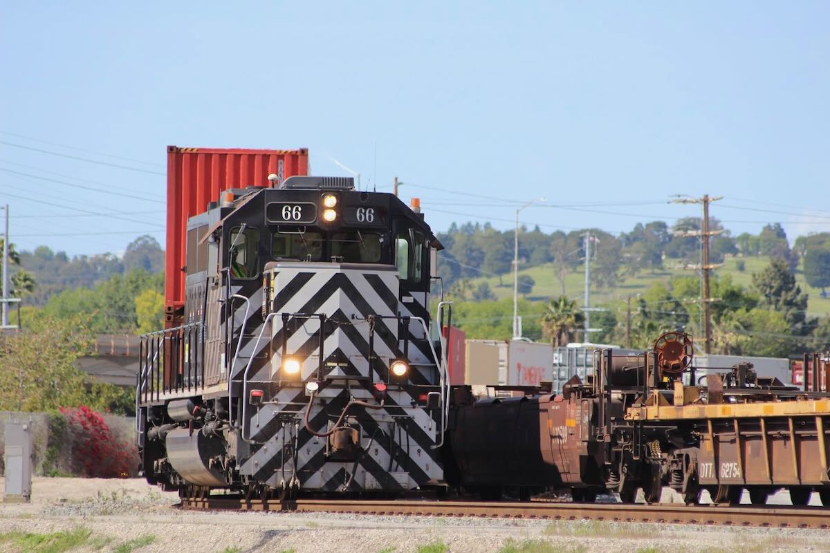 Black locomotive with white nose striping moves double-stack cars