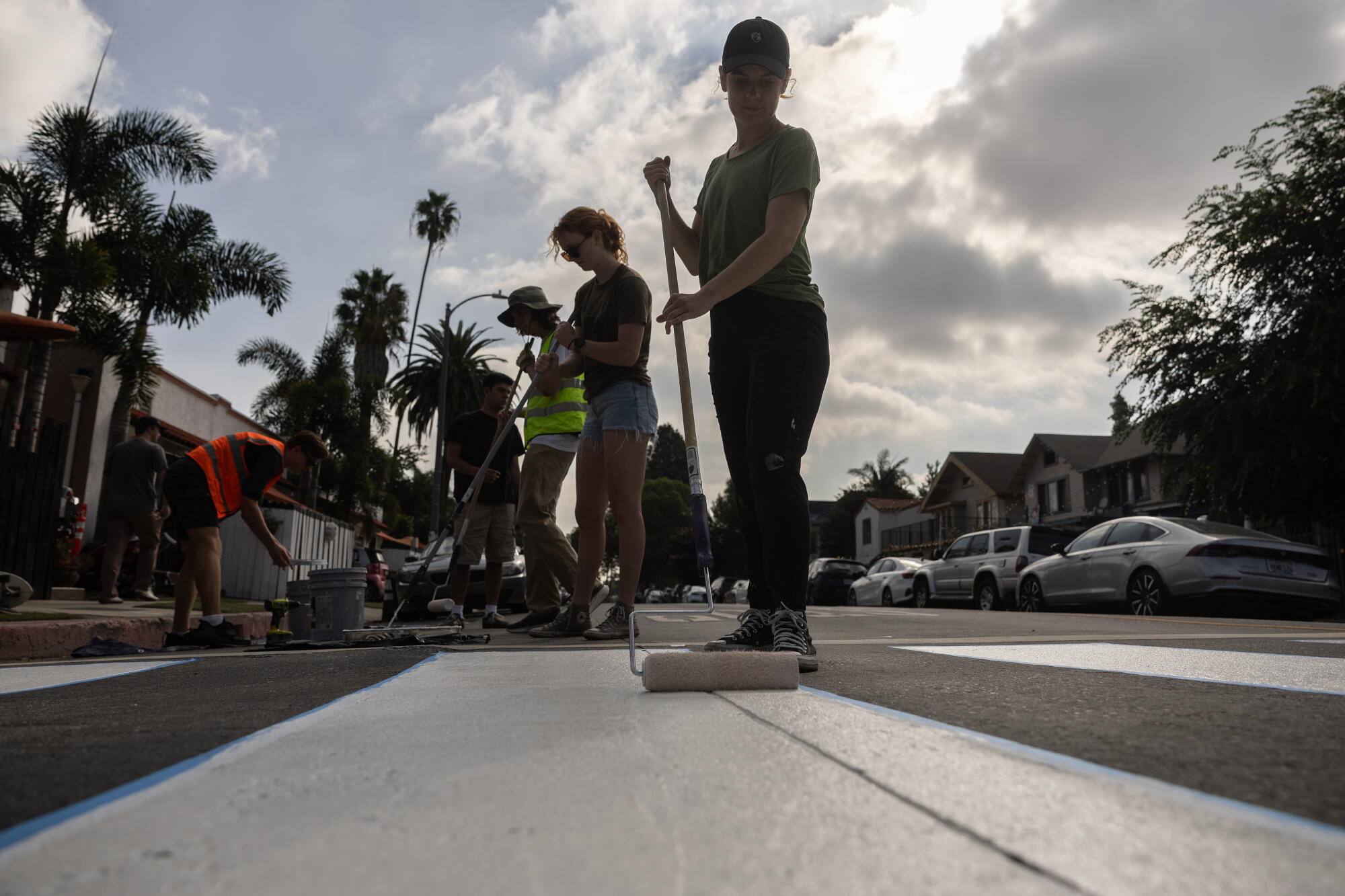 A woman uses a long roller brush to paint a white stripe on a street.