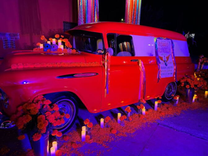 A red truck decorated in flowers, candles, and a poster at night.
