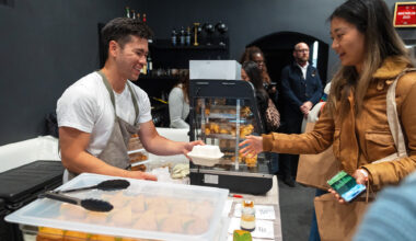 Asian man in a chef's apron hands baked goods to a customer.