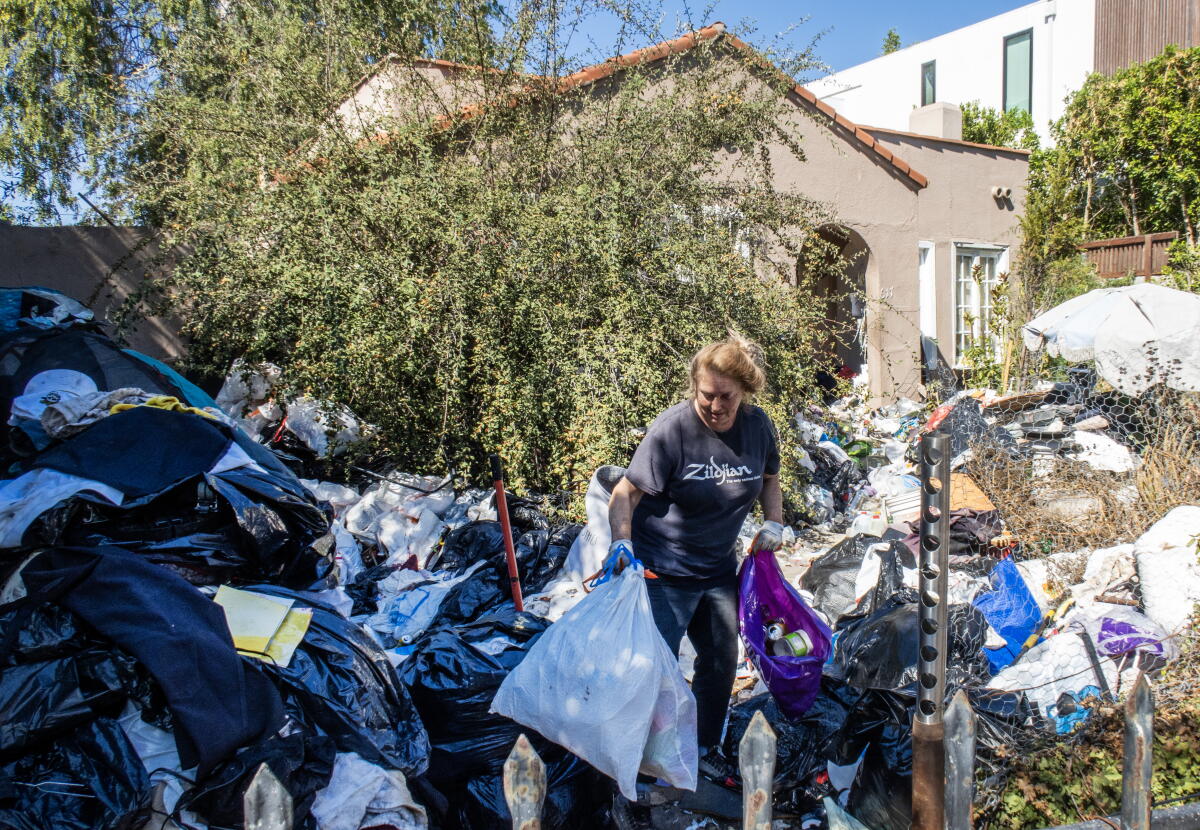 A woman helps clean up a yard, gathering and bagging recyclables 