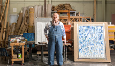 older Korean man in denim overalls next to abstract painting