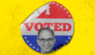 A round sticker with "I VOTED" in red, set against a patriotic red, white, and blue background with stars. A smiling man's grayscale face is at the bottom.
